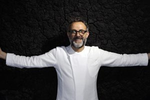 Fotografia di Massimo Bottura a braccia apertesu sfondo nero