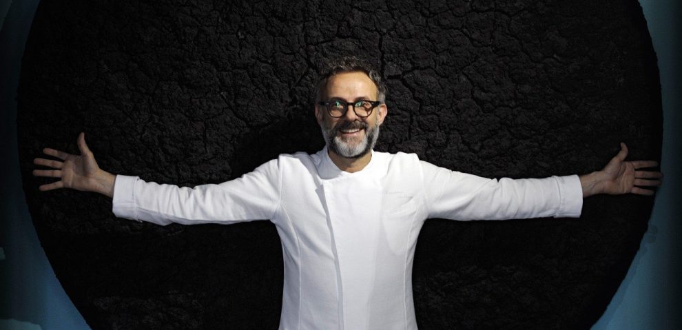Fotografia di Massimo Bottura a braccia apertesu sfondo nero