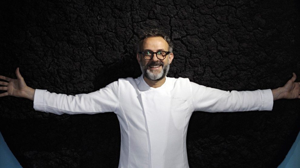 Fotografia di Massimo Bottura a braccia apertesu sfondo nero
